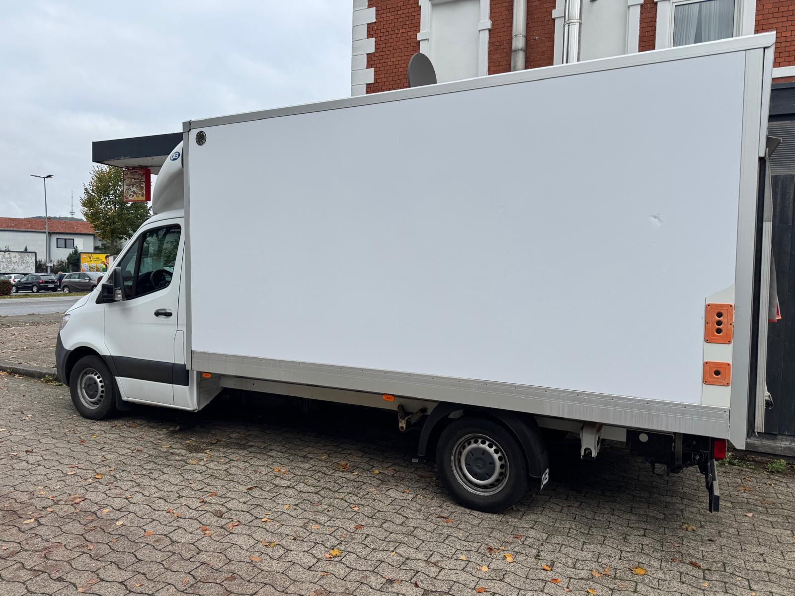 Weißer Transporter mit Kofferaufbau vor einem Gebäude.