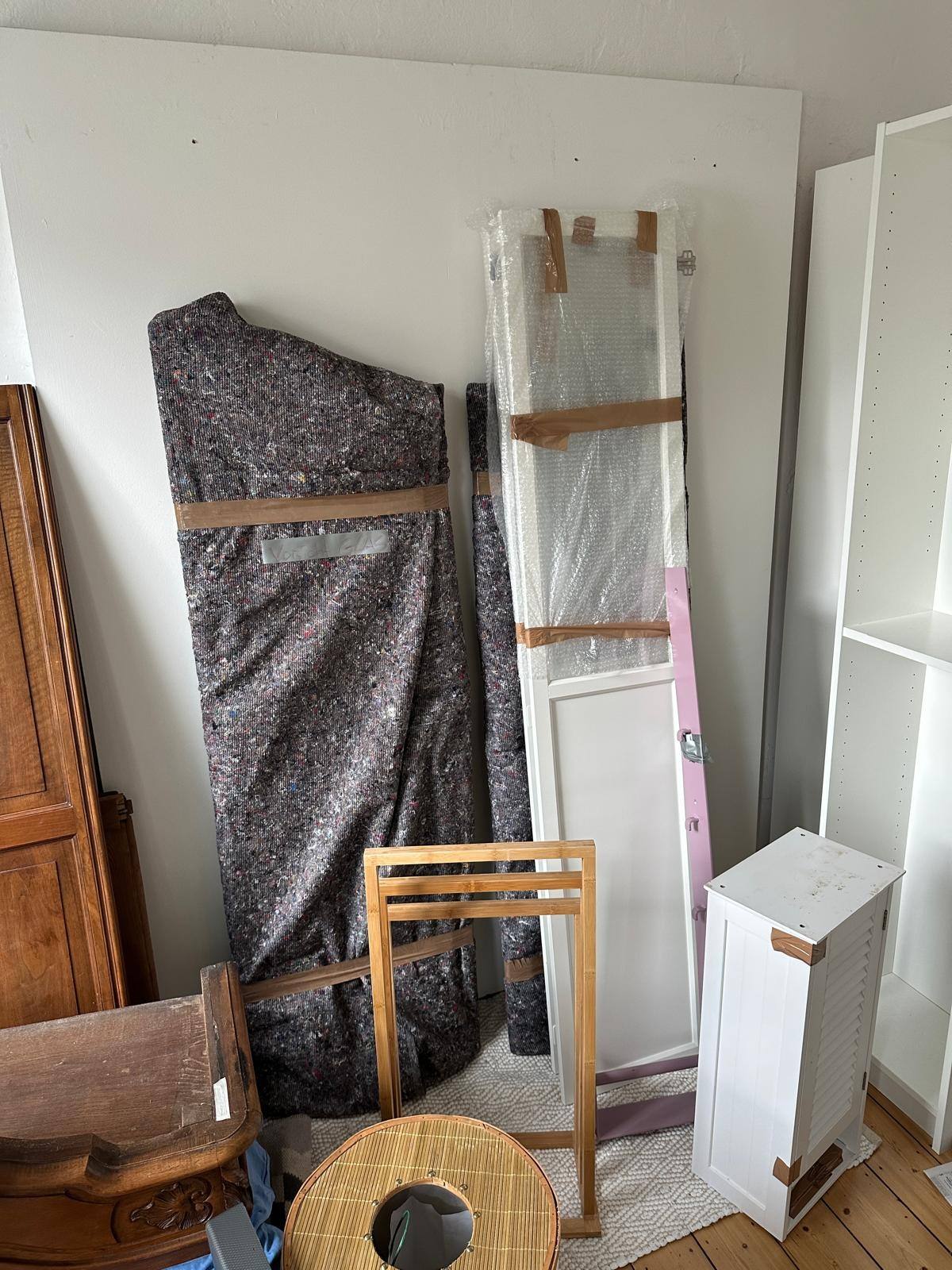 Möbelteile, in graue Umzugsdecken eingewickelt und mit Klebeband gesichert, lehnen an einer Wand.